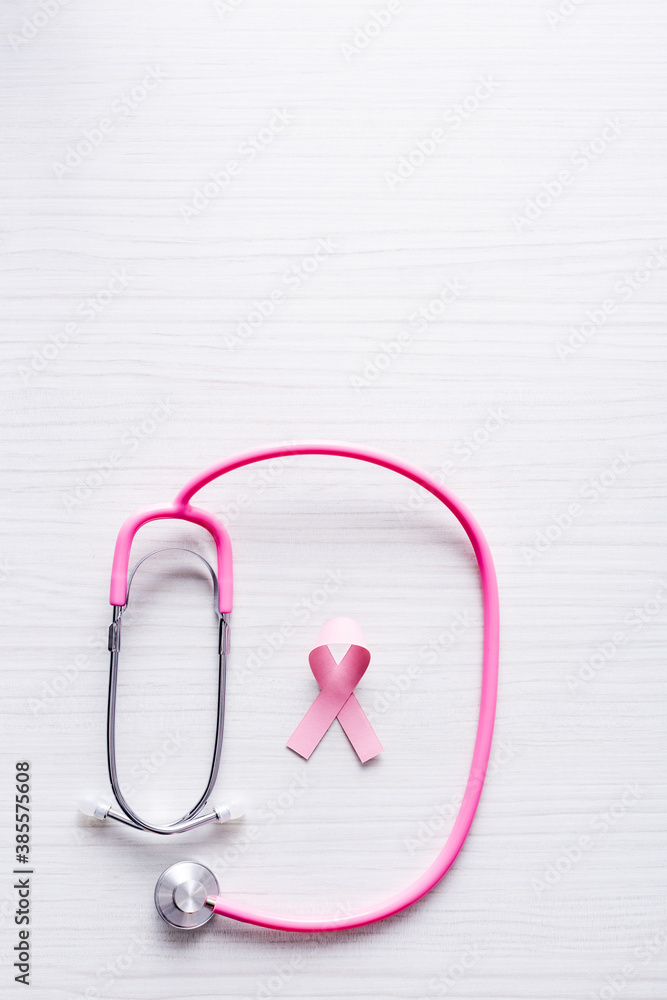 Top view of ribbon of breast cancer awareness and stethoscope on white wooden background