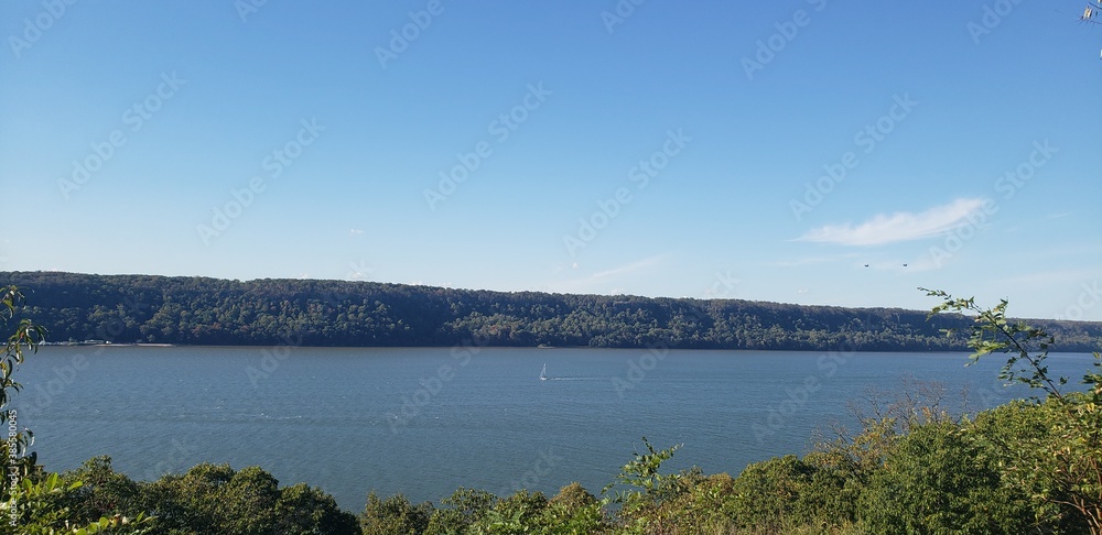 Obraz premium Hudson River viewed at a distance off a vista in Northern Manhattan's Inwood Hill Park. On the river can be seen a sail boat, small at this distance.