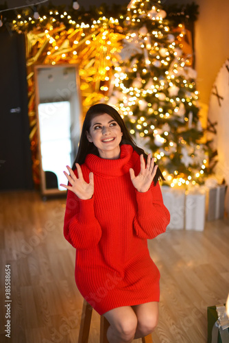 In Christmas room, surprised beautiful girl wearing in red Christmas sweater,her hands are up.