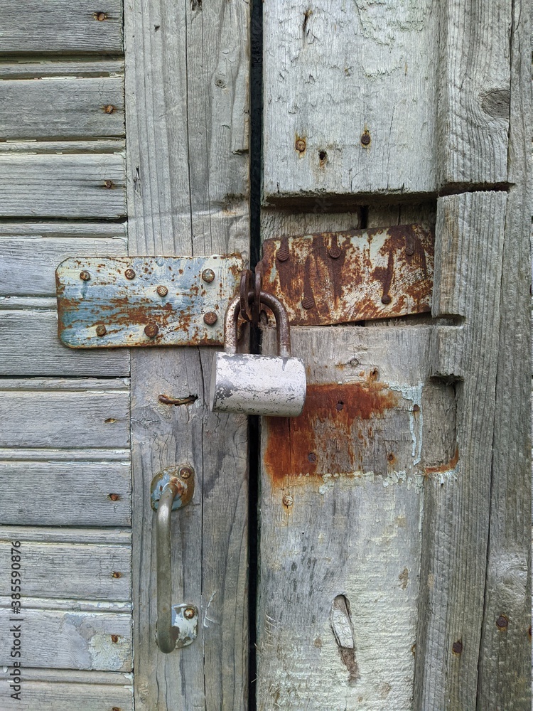 powerful steel and rusty closed padlock on a wooden barn door powerful steel and rusty closed padlock on a wooden barn door