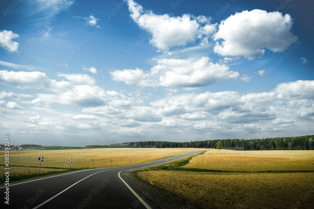 Road between yellow fields. Landscape with blue skue and big clouds.