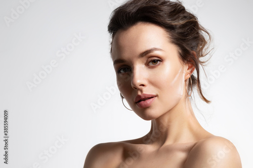 Close up of beautiful young woman with healthy soft glowing skin and bare shoulders in studio isolated on white background. Advertising poster for skincare cosmetics and rejuvenation procedure photo