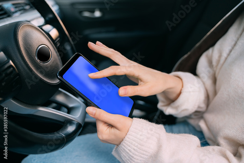 The girl in the car holds a smartphone in her left hand. Clicks with his right hand on the smartphone screen. Blue screen. Template