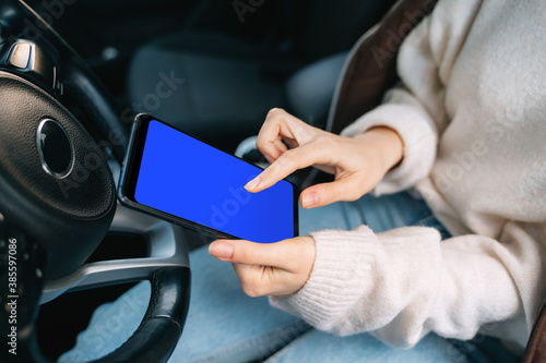A young girl holds a smartphone sitting in a car. Gadget in hand, touch screen, template for your design.