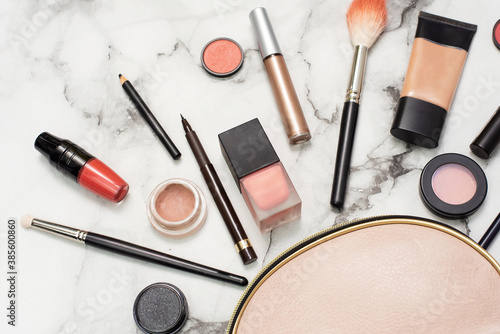 Beautician on a marble background with a makeup brush, tonal foundation, lipstick, lip liner, blush and eye shadow. The concept of expensive luxury cosmetics