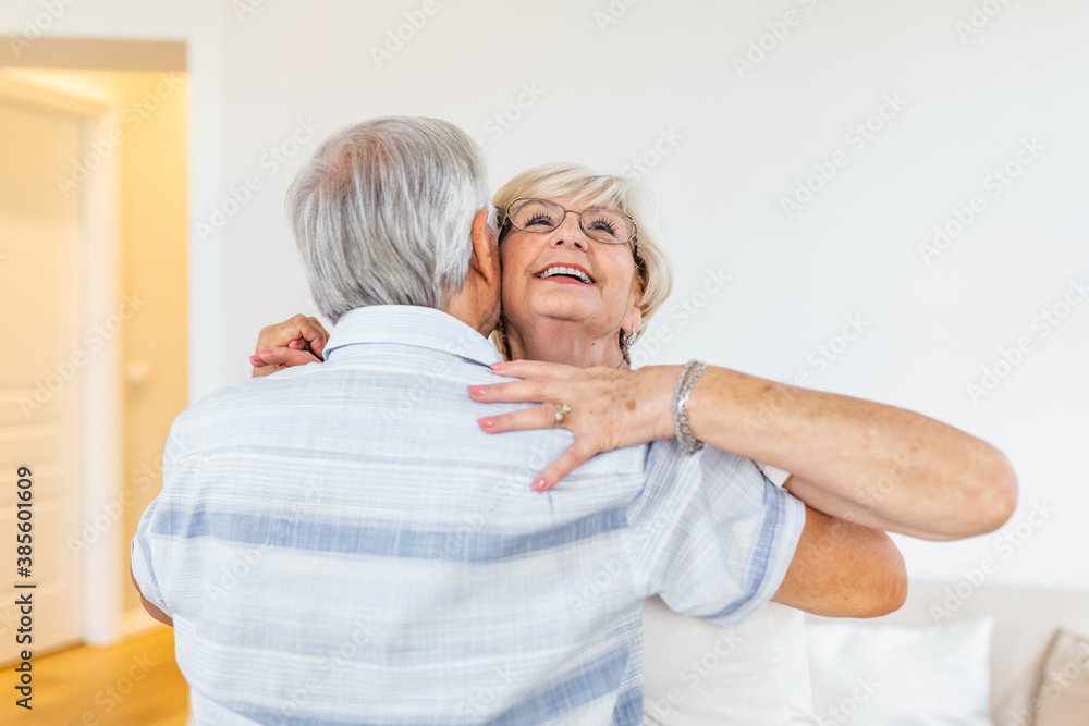 Head shot portrait smiling older woman dancing with man, happy mature wife and husband hugging, standing in living room, senior family enjoying tender moment, celebrating anniversary Head shot portrait smiling older woman dancing with man, happy mature wife and husband hugging, standing in living room, senior family enjoying tender moment, celebrating anniversary