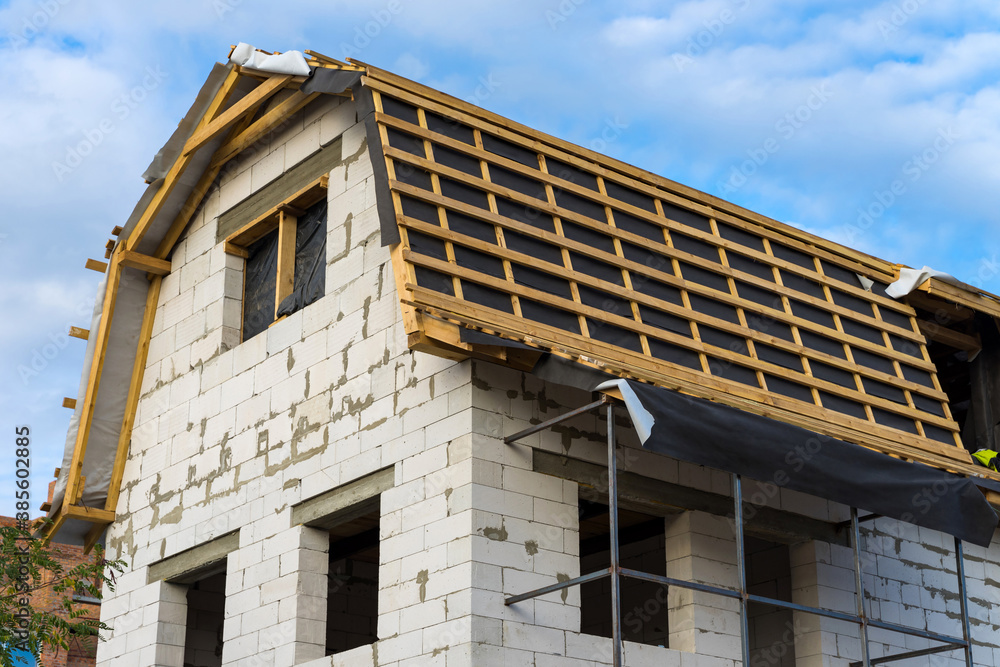 Installation of wooden beams and vapor barrier at construction the roof truss system of the house. New residential construction home framing. Installation of wooden beams and vapor barrier at construction the roof truss system of the house. New residential construction home framing.