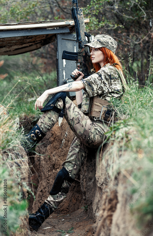 Sniper girl in a green field. Military snipers. The sniper smokes. Red-haired girl in camouflage. Fighting