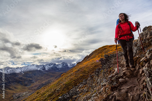 Woman Backpacking along Scenic Hiking Trail surrounded by Mountains in Canadian Nature. Season change from Fall to Winter. Taken in Tombstone Territorial Park, Yukon, Canada.