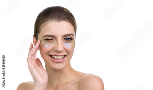 Beautiful young woman applies holographic, moisturizing eye mask, isolated on white.