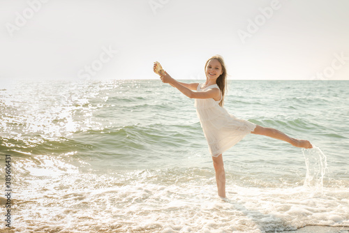 Portrait of beautiful little girl is playing with seashell in sea waves. © jutaphoto