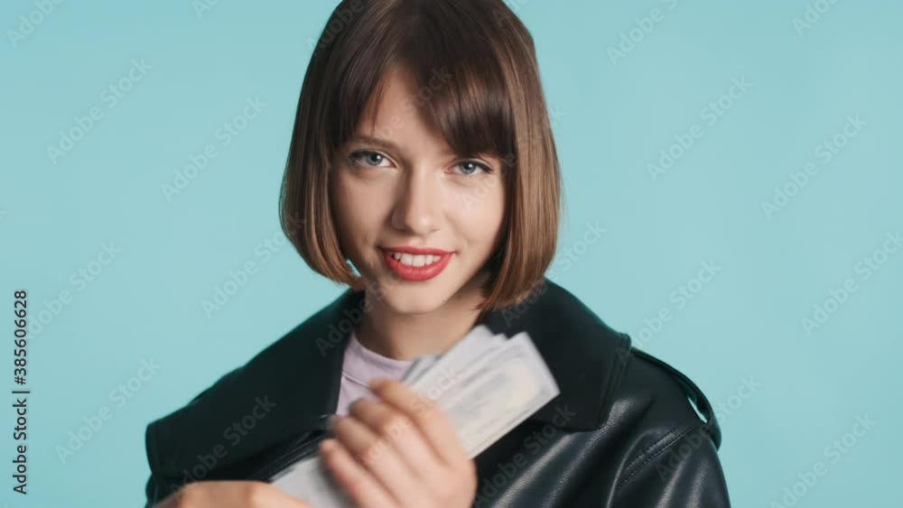 Beautiful stylish brunette girl with bob hair dressed in casual wear waving wide of money confidenly posing on camera over colorful background. Successful concept Beautiful stylish brunette girl with bob hair dressed in casual wear waving wide of money confidenly posing on camera over colorful background. Successful concept
