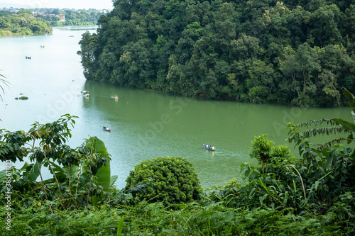 View of a tropical lake surrounded by lush green vegetation. Many small boats with tourists float on the surface of the water