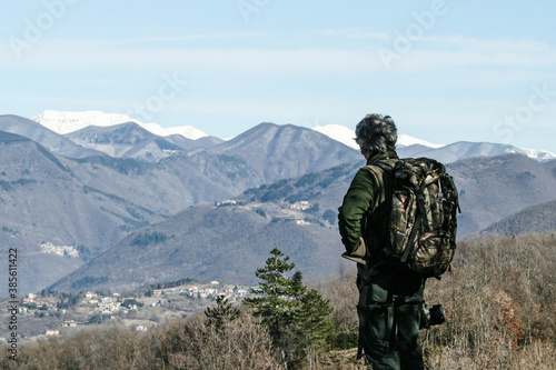 Hiker senior man with backpack standing on the mountain top - Active traveler pensioner with grey hair - Discovery travel destination concept - copy space  main focus on the left  on the man