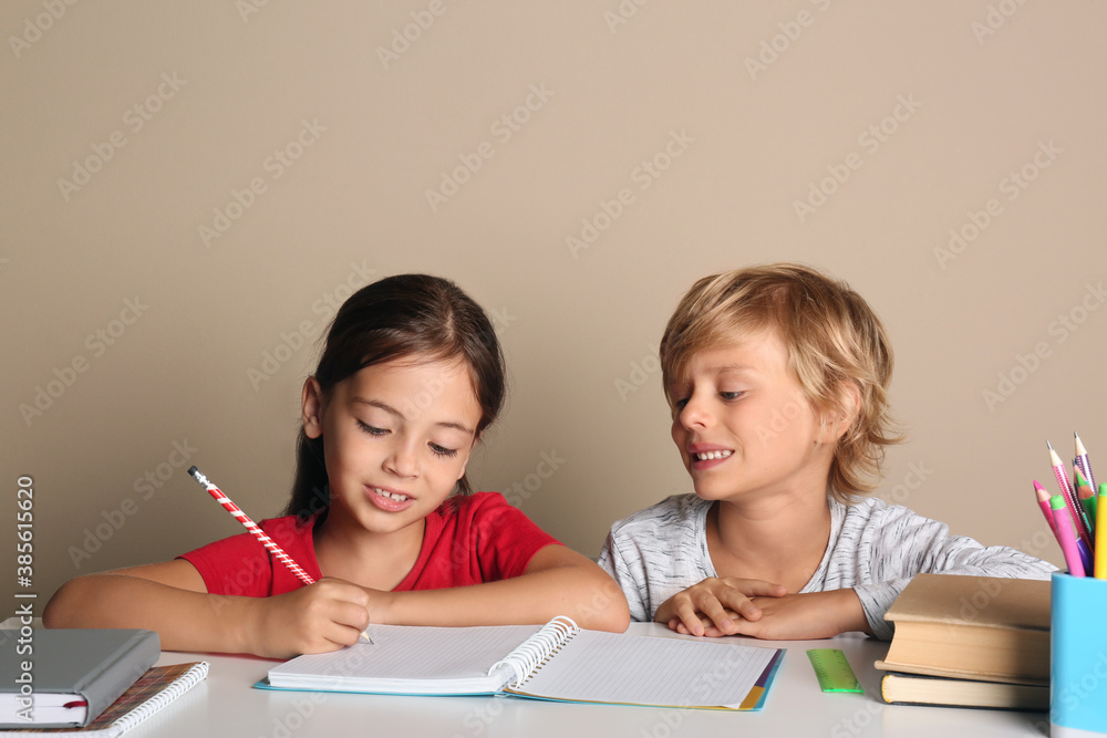 Little boy and girl doing homework at table on beige background Little boy and girl doing homework at table on beige background