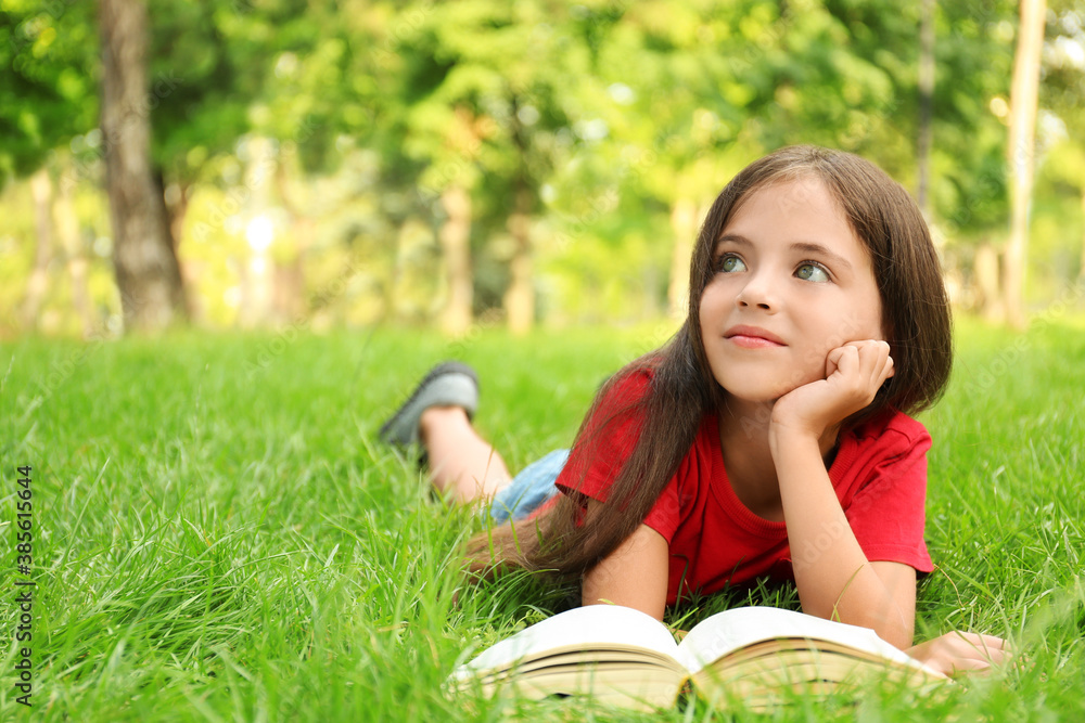Cute little girl reading book on green grass in park Cute little girl reading book on green grass in park