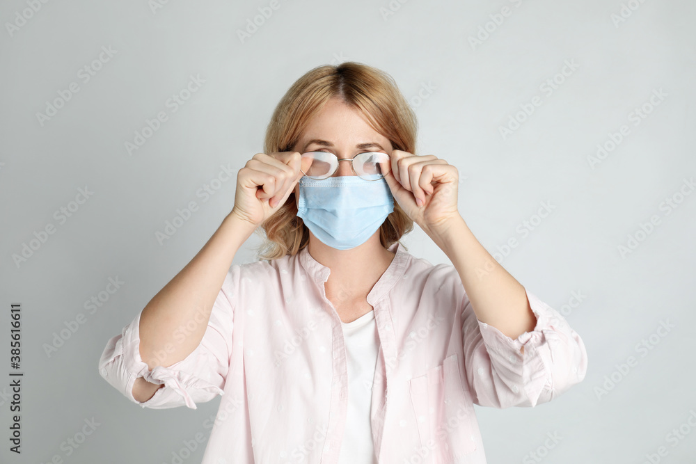Woman wiping foggy glasses caused by wearing medical mask on light background Woman wiping foggy glasses caused by wearing medical mask on light background