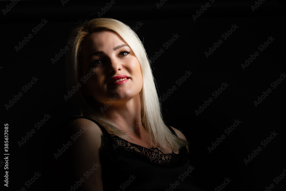 Young beautiful blond glamorous woman in black over dark background