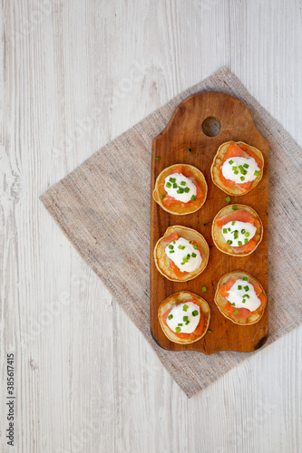 Homemade Blini with Smoked Salmon, Creme and Chives on a rustic wooden board, top view. Flat lay, overhead, from above. Copy space.