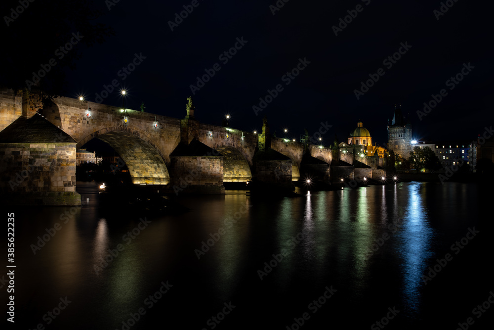 illuminated by the light of Charles Bridge. monument from 1402 in the center of prague on the flowing river vltava in the czech republic paving blocks for sidewalks and light from street lighting on 