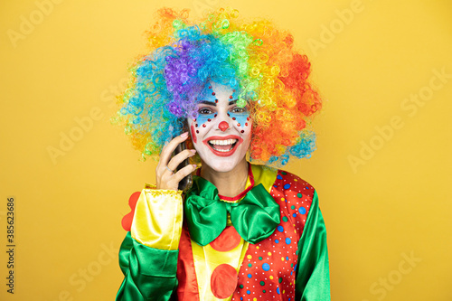 Clown standing over yellow insolated yellow background smiling and talking on the phone