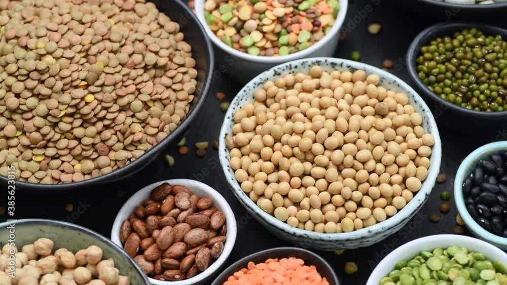 Legumes, soya, lentils, chickpeas and beans assortment in various bowls on black stone background, rotating Legumes, soya, lentils, chickpeas and beans assortment in various bowls on black stone background, rotating