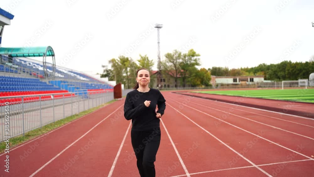 Young active woman running on fresh air at stadium. Adult fit female in sportswear running on red track at outdoor stadium. Concept of healthy lifestyle. Young active woman running on fresh air at stadium. Adult fit female in sportswear running on red track at outdoor stadium. Concept of healthy lifestyle.