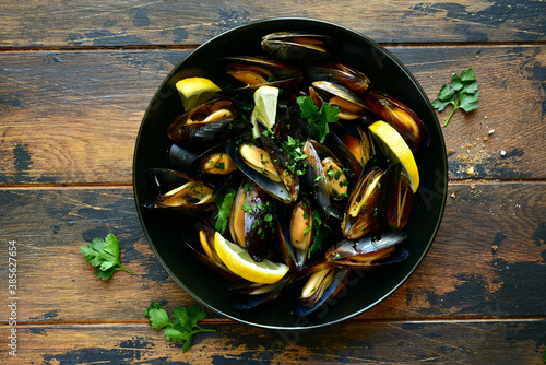 Boiled mussels with lemon and parsley in a black bowl. Top view with copy space.