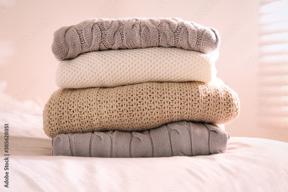 Stack of folded warm sweaters on bed indoors