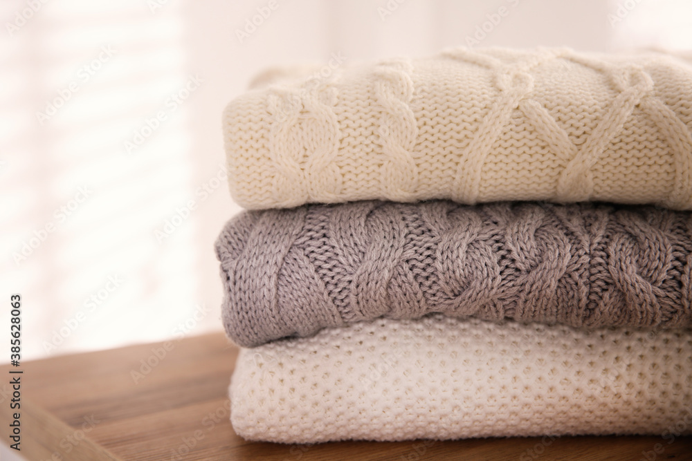 Stack of folded warm sweaters on wooden table indoors, closeup