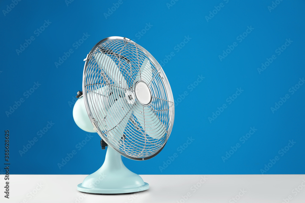 Electric fan on white table against blue background, space for text. Summer heat