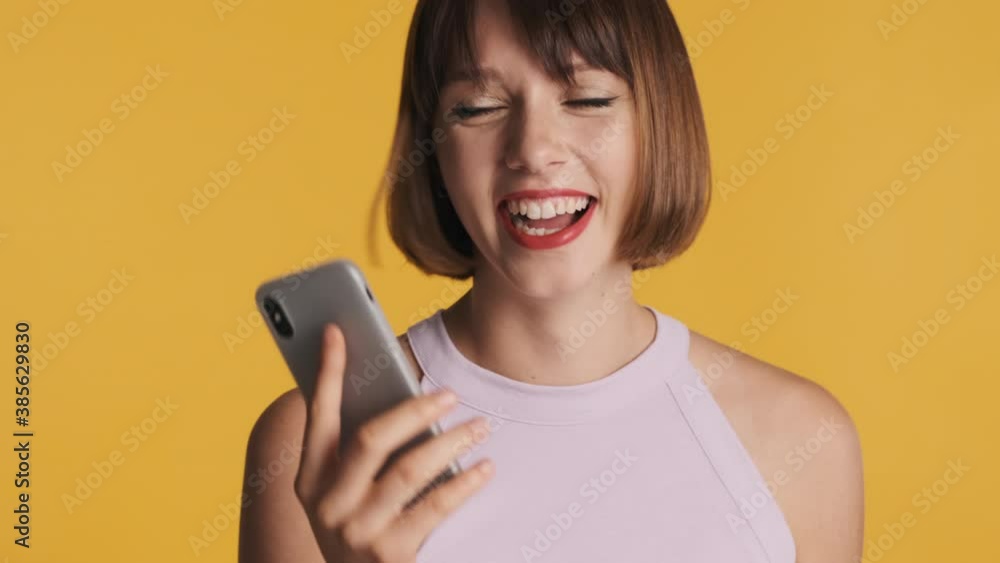Cheerful brunette girl with bob hair happily laughing talking with friend on smartphone over yellow background. Overjoyed expression Cheerful brunette girl with bob hair happily laughing talking with friend on smartphone over yellow background. Overjoyed expression