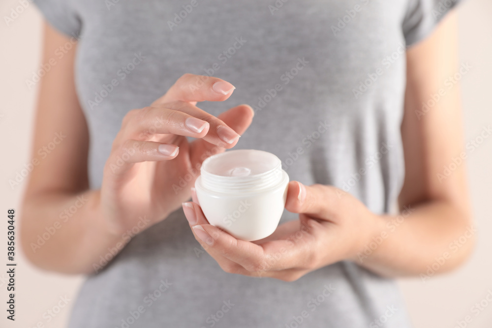 Young woman holding jar of cream on light background, closeup Young woman holding jar of cream on light background, closeup