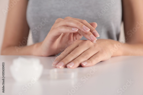 Young woman applying hand cream at table, closeup