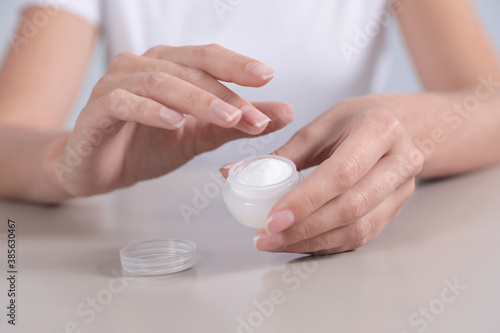 Young woman holding jar of cream at table, closeup