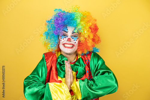 Clown standing over yellow insolated yellow background begging and praying with hands together with hope expression on face very emotional and worried