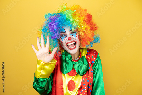 Clown standing over yellow insolated yellow background showing and pointing up with fingers number five while smiling confident and happy