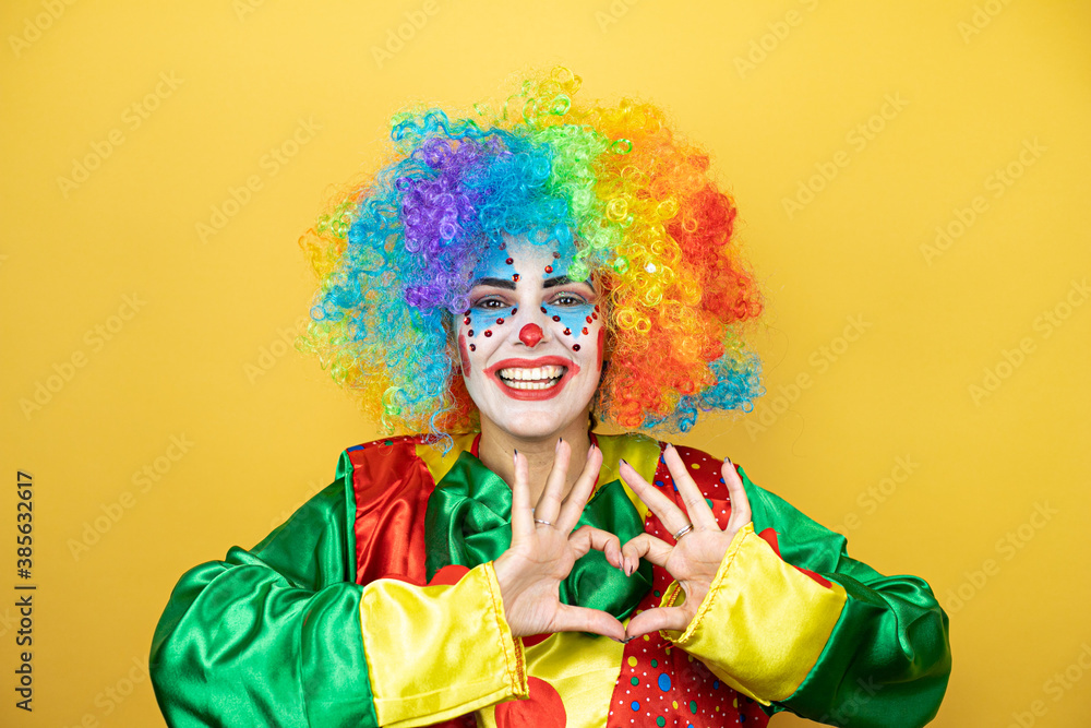 Clown standing over yellow insolated yellow background smiling in love showing heart symbol and shape with hands Clown standing over yellow insolated yellow background smiling in love showing heart symbol and shape with hands
