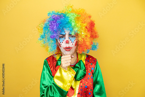 Clown standing over yellow insolated yellow background with her hand to her mouth because she's coughing