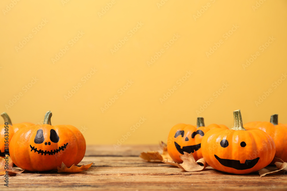 Pumpkins with scary faces and fallen leaves on wooden table against yellow background, space for text. Halloween decor - obrazy, fototapety, plakaty 
