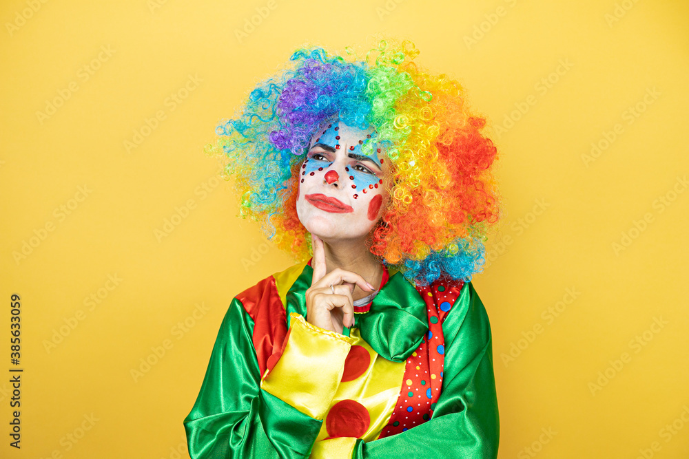 Clown standing over yellow insolated yellow background thinking and looking to the side Clown standing over yellow insolated yellow background thinking and looking to the side