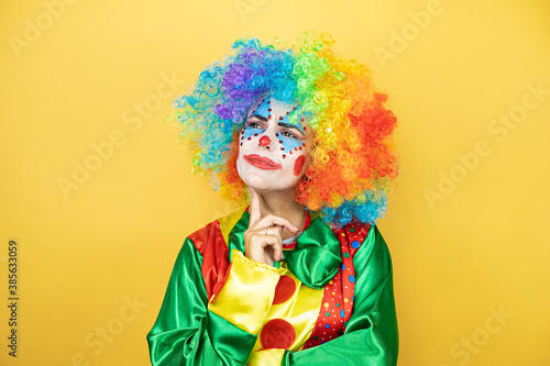 Clown standing over yellow insolated yellow background thinking and looking to the side