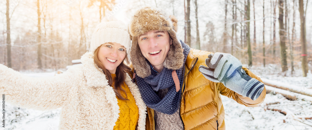 Obraz premium happy loving couple walking in snowy winter forest, spending christmas vacation together. Outdoor seasonal activities