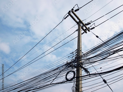 High voltage transmission lines on concrete poles. Below are low voltage and communication cables along with Guy Wire. On a white cloud sky background. Selective focus