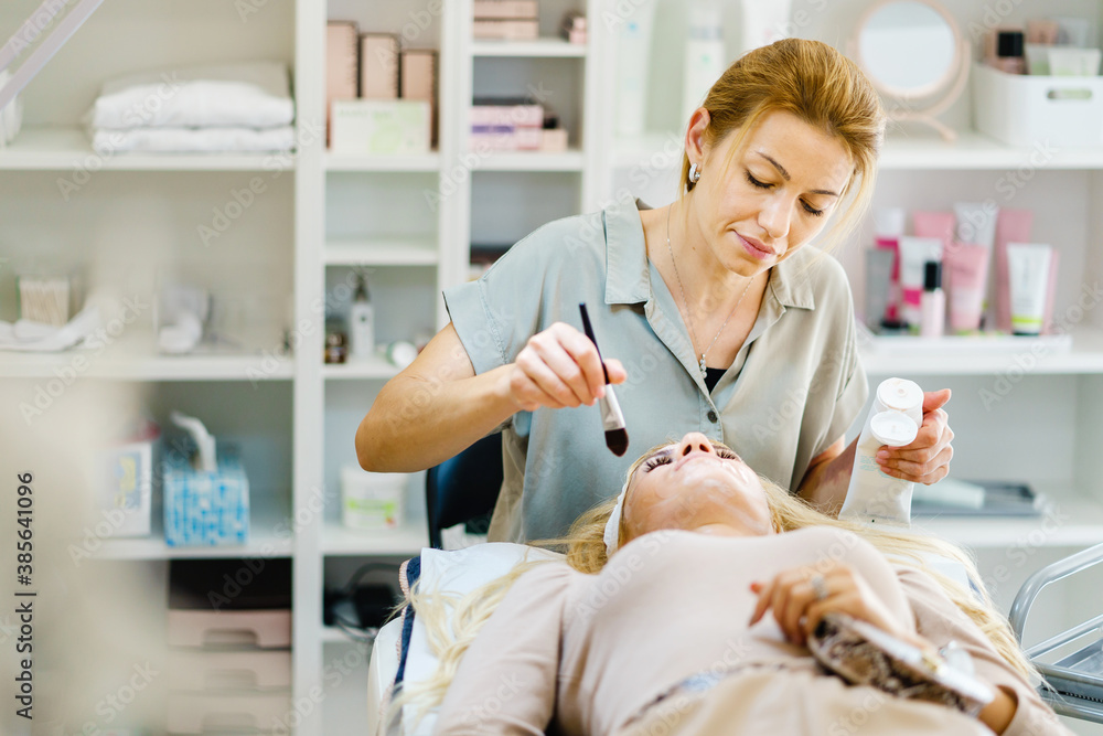 Beautiful happy caucasian woman smiling while doing face treatment to client at spa - Female beautician doctor cosmetologist applying face mask with brush at salon - healthcare concept copy space Beautiful happy caucasian woman smiling while doing face treatment to client at spa - Female beautician doctor cosmetologist applying face mask with brush at salon - healthcare concept copy space