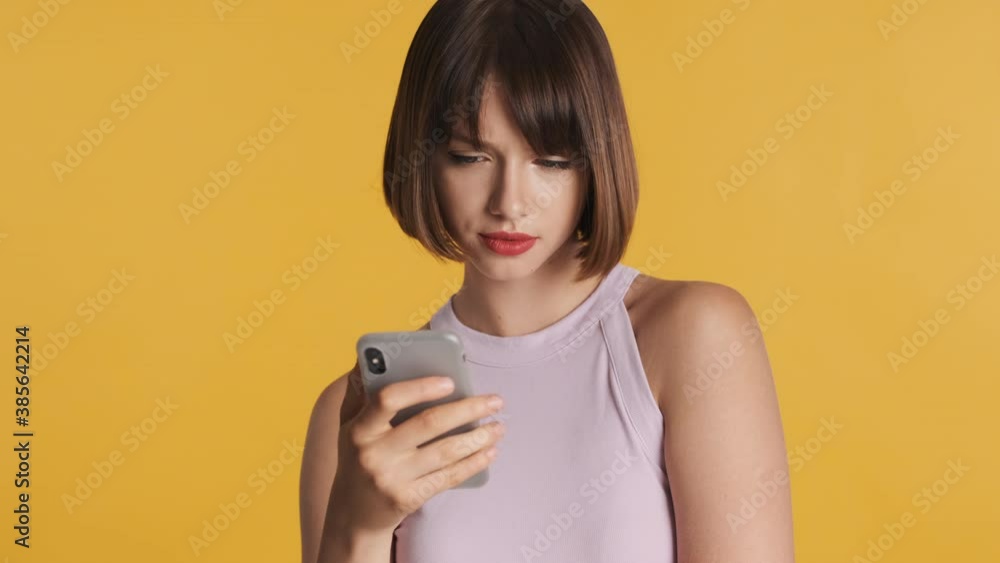 Serious brunette girl with bob hair and red lips browsing social networks using smartphone over colorful background Serious brunette girl with bob hair and red lips browsing social networks using smartphone over colorful background