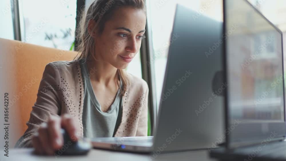 Young smiling business woman working on portable laptop computer. Female copywriter sitting at desk and scrolling mouse, searching, surfing or looking content at laptop Young smiling business woman working on portable laptop computer. Female copywriter sitting at desk and scrolling mouse, searching, surfing or looking content at laptop