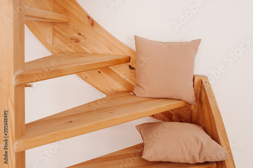 two beige pillows made of natural fabric on a wooden spiral staircase in the house. Cozy natural home decor  selective focus