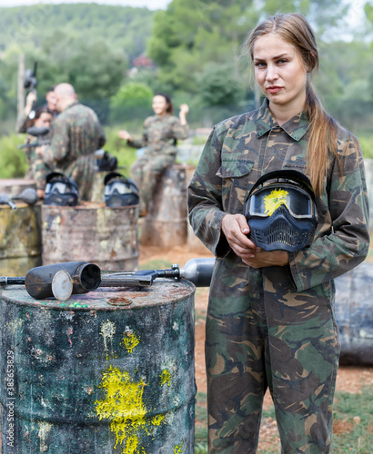 sad female paintball player standing with black mask with traces of paint from hit markers after match