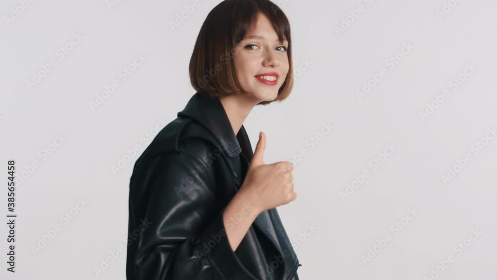 Pretty girl with bob hair dressed in leather jacket keeping thumb up saying it's cool over white background. Body language concept Pretty girl with bob hair dressed in leather jacket keeping thumb up saying it's cool over white background. Body language concept